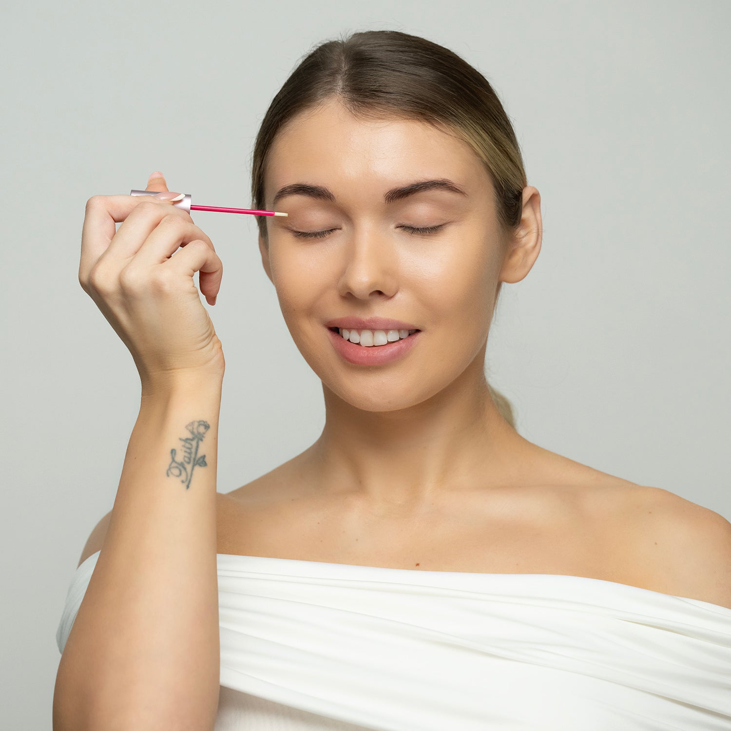 Woman applying makeup with a brush on a plain background