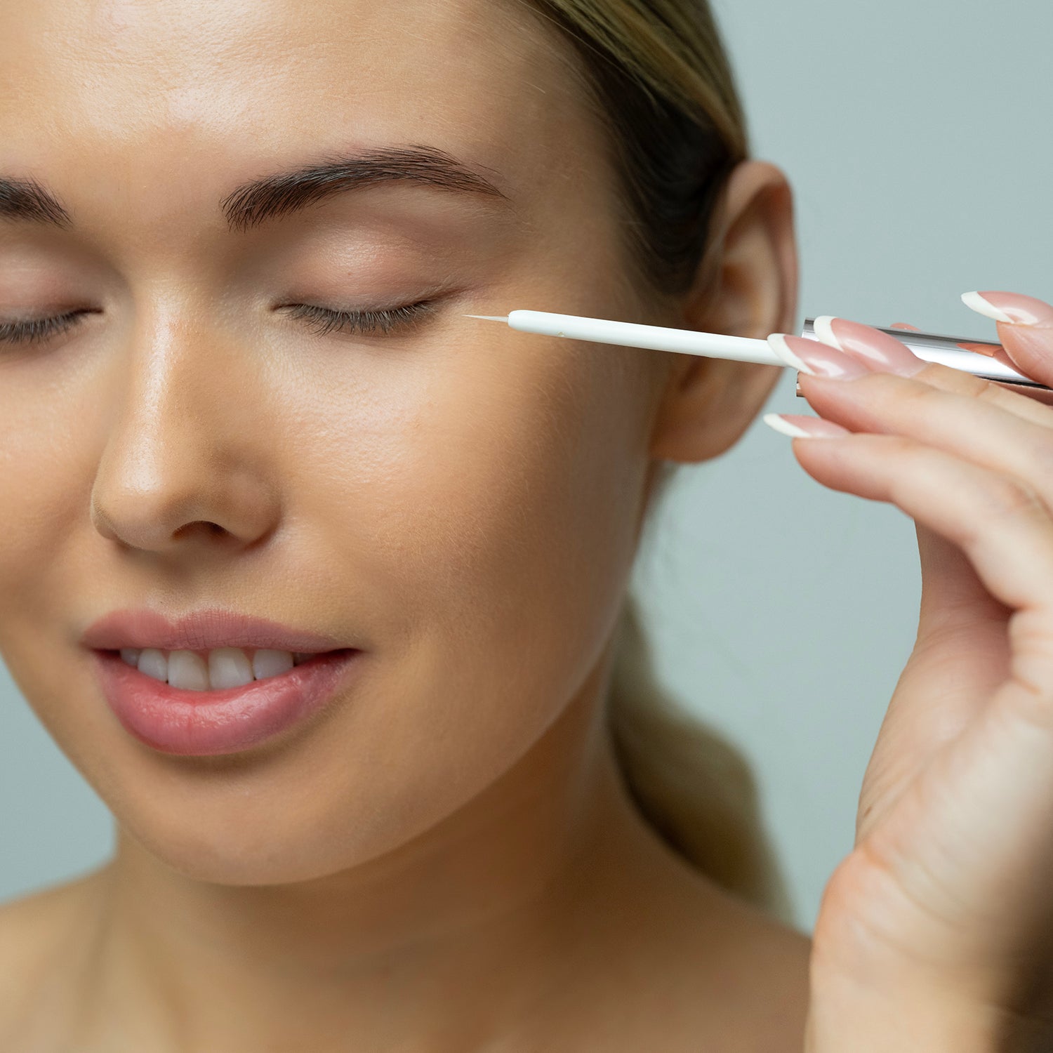 Woman applying eyelash growth serum with a brush on a neutral background