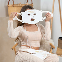Woman holding the Lerelle Beauty LED light therapy face mask before putting it on, with neck and décolletage mask visible