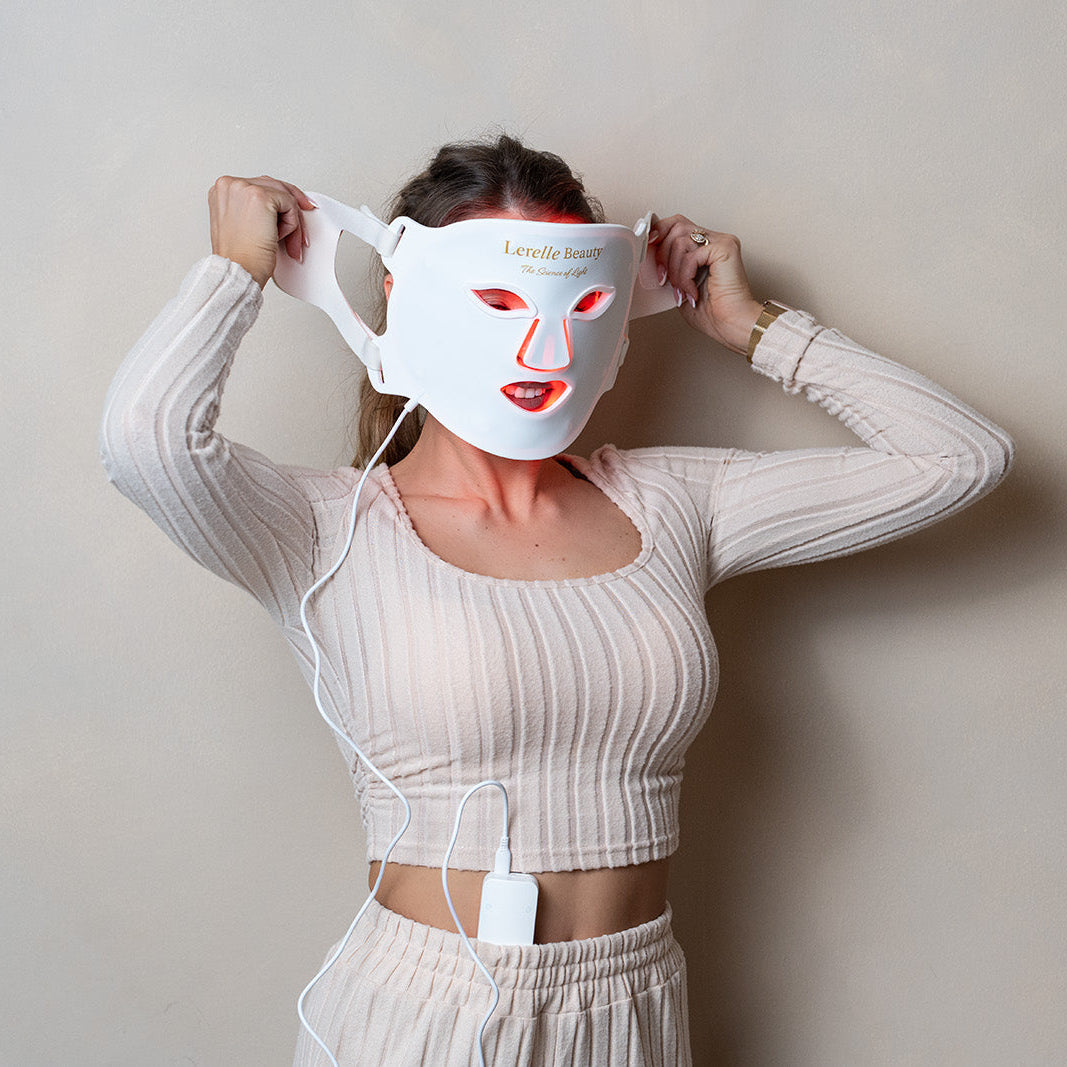 Woman adjusting the straps of the Lerelle Beauty red light therapy face mask, red LEDs glowing around the eyes and mouth