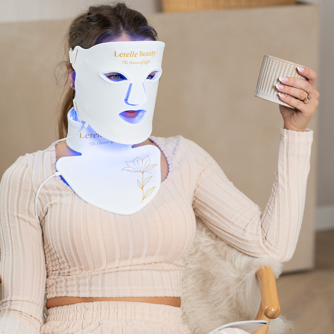 Lerelle Beauty LED light therapy face, neck and décolletage mask worn while sitting and holding a mug