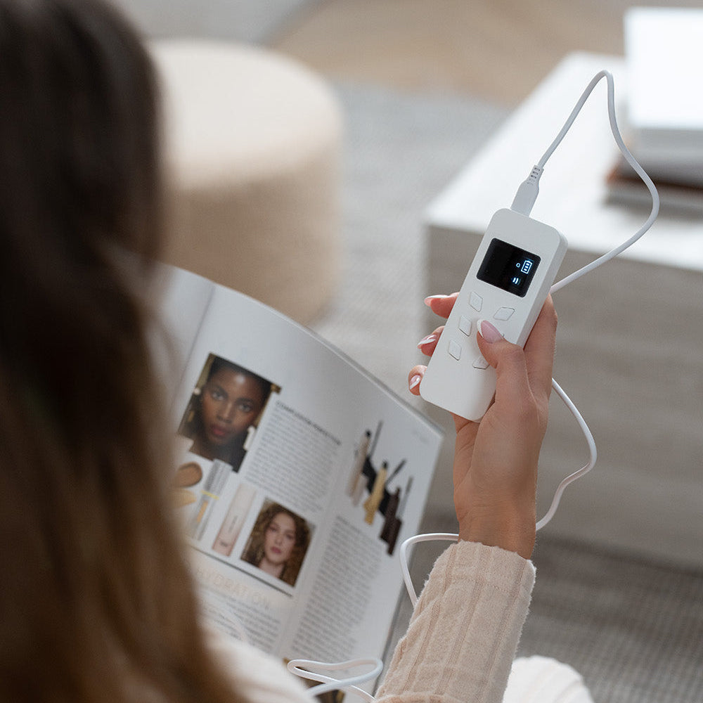 Woman holding the Lerelle Beauty LED face mask remote control while reading a magazine