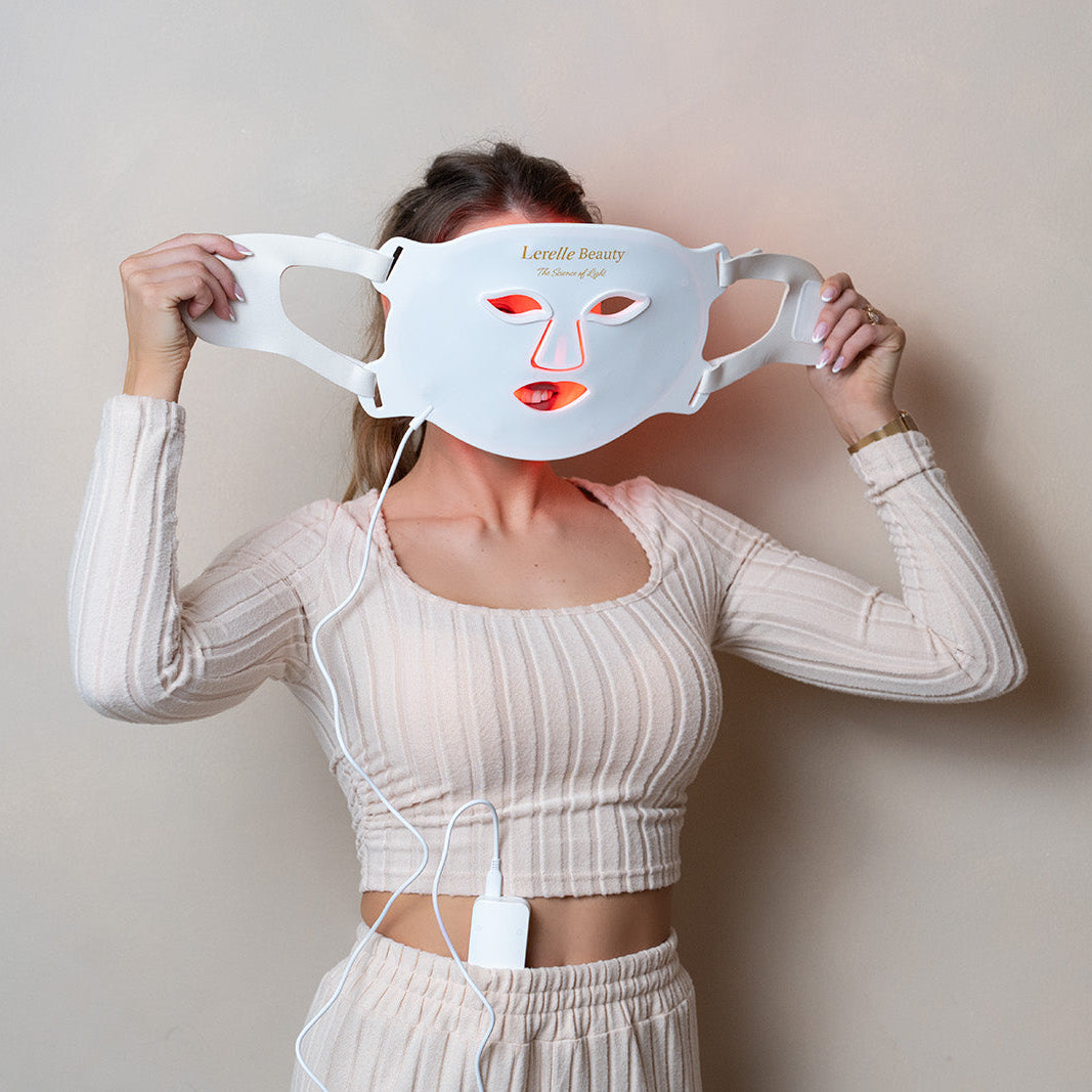 Woman adjusting Lerelle Beauty LED light therapy face mask straps in red light mode