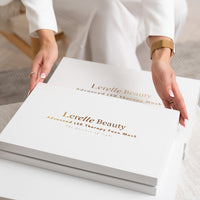 Woman placing the Lerelle Beauty red light therapy face mask gift box on a table, two boxes stacked together